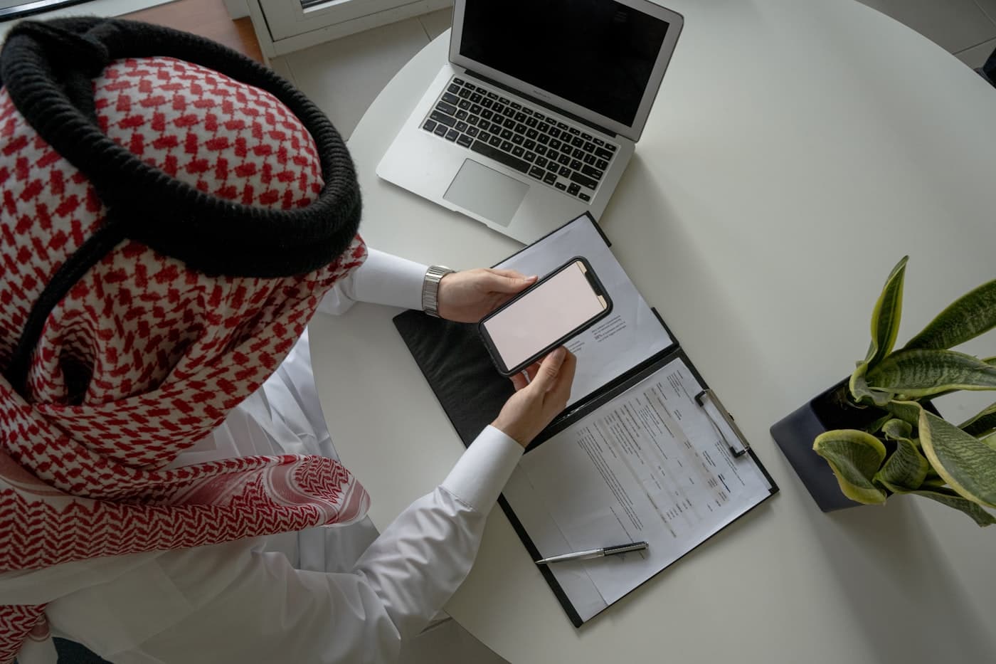 A founder in traditional Gulf dress reviewing plans at a laptop in the studio